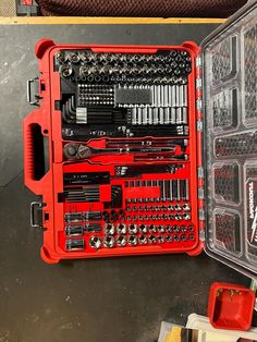 a red tool box filled with tools on top of a metal table next to other tools