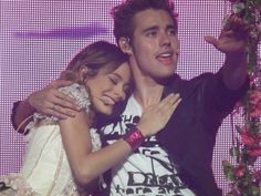 a man and woman hugging each other on stage with flowers in front of the camera