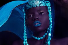 an african woman with blue makeup and beads on her head, wearing a turquoise hat