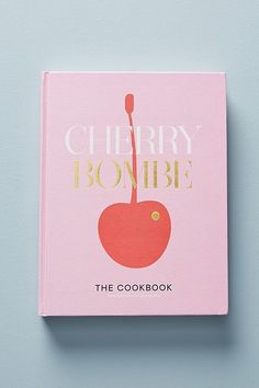 the cherry bombe cookbook is shown on a light blue surface with gold lettering