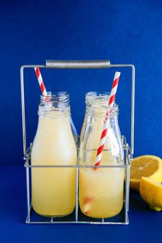 two lemonade drinks in glass bottles with red and white striped straws next to an orange slice