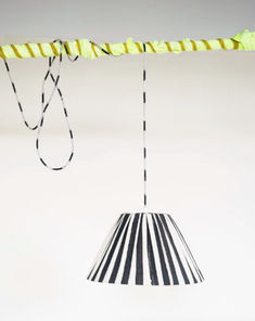 a black and white striped lamp shade hanging from a string with yellow strips on it