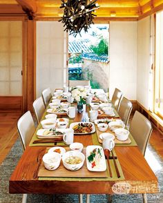 a dining room table set with plates and bowls on top of it, in front of an open window