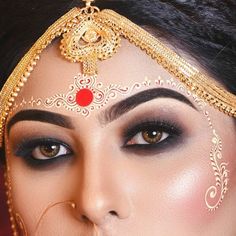 a close up of a woman with makeup on her face and gold jewelry around her eyes