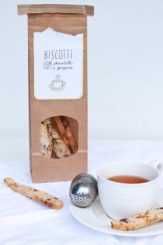 a cup of tea and some cookies on a white plate with a box of biscotti in the background