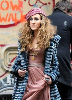 a woman in a dress and jacket walking down the street with graffiti on the wall behind her