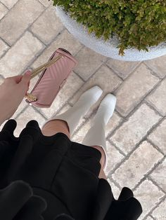 a woman is holding a pink purse and wearing white high - heeled shoes with her legs crossed