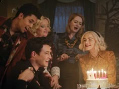 a group of people standing around a cake with lit candles