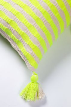 a yellow and white striped pillow with tassels on the bottom, sitting on a table