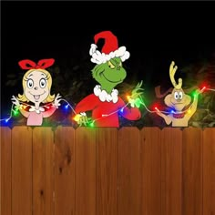 three cartoon characters are standing behind a fence with christmas lights