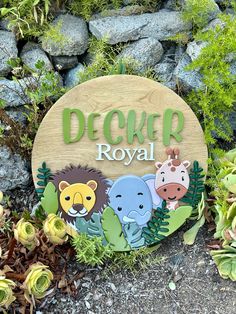 a wooden sign that says decker royal with cartoon animals on it next to flowers and rocks