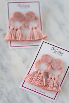 two pink buttons with tassels sitting on top of a white card next to each other