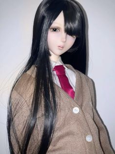 a doll with long black hair wearing a brown jacket and red tie, standing in front of a white wall