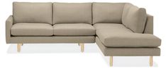 a beige sectional couch sitting on top of a white floor next to a wooden leg chair