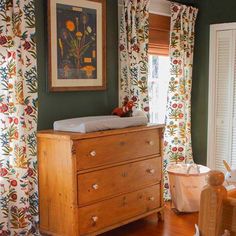 a baby crib in the corner of a room with green walls and floral curtains