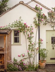 a small white house with pink flowers growing on the front and side of it's door