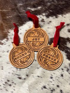 three wooden medallions with red ribbons on a cowhide background, one has the word joy written in it