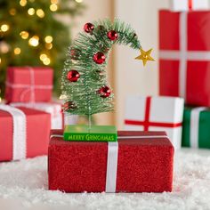 a small christmas tree sitting on top of a red present box next to a pile of presents