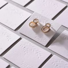 two wedding rings sitting on top of white cards with embellishments in them