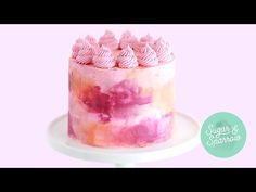 a cake with pink frosting and icing on a white platter against a pink background