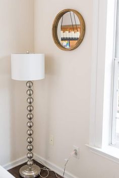 a room with a lamp on the floor and a mirror hanging on the wall above it