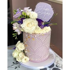 a purple and white cake with flowers on it sitting on a table next to a sign that says happy birthday mom