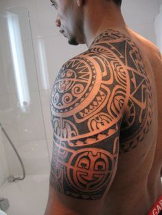 a man with a tattoo on his arm and shoulder in front of a bathtub