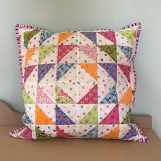 a colorful pillow sitting on top of a wooden table next to a white vase with flowers in it