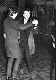 an old photo of two people dancing in a room with tile floors and walls, one man is holding the other woman's hand