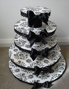 three tiered cake with black bows on top, sitting on the floor in front of a wall