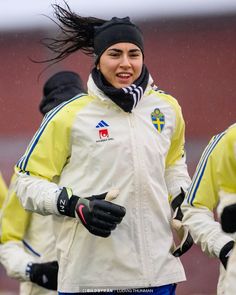 a woman in white jacket and blue pants running on snow covered ground with other people behind her