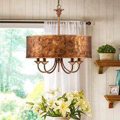 a chandelier hanging from the ceiling over a table with flowers on it in front of a window