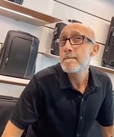 an older man wearing glasses and a black shirt is standing in front of some suitcases