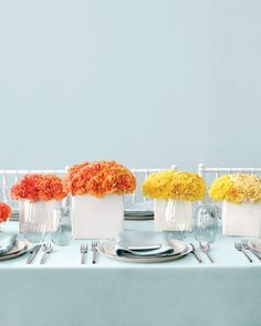 an arrangement of flowers in vases on a white table cloth with silverware and napkins