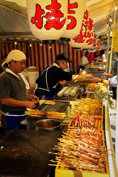 two men preparing food on sticks at an outdoor market