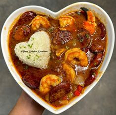 a heart shaped bowl filled with shrimp, rice and broth next to a person's hand