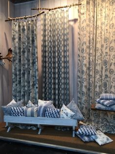 a bed with blue and white pillows on top of it in front of curtained windows