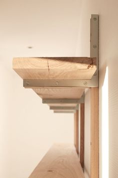 a wooden shelf with metal brackets on the bottom and sides in a white walled room