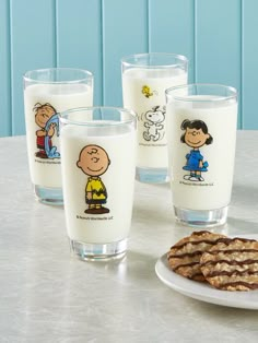 three glasses filled with milk, cookies and peanuts on a table next to blue wall