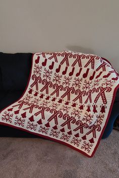 a red and white crocheted afghan sitting on top of a blue couch next to a black pillow