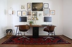 two chairs sitting at a desk in front of pictures on the wall