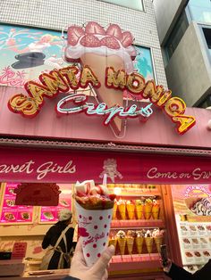 a person holding up an ice cream sundae in front of a storefront with the name santa monica cafe on it