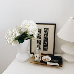 a white vase filled with flowers sitting on top of a table next to a lamp