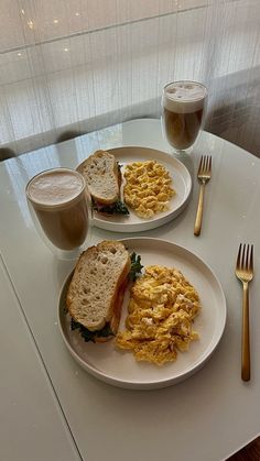 two white plates topped with sandwiches and scrambled eggs next to a cup of coffee on a table