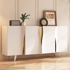 a white cabinet with gold legs and a clock next to it on a wooden floor