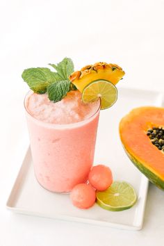 a fruit smoothie is garnished with mint and lime on a white plate