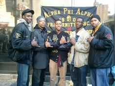 four men are standing together in front of a black banner with gold letters on it