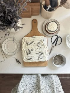 an overhead view of a cake on a cutting board with lavenders and other items around it