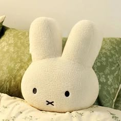 a white stuffed rabbit sitting on top of a bed next to pillows and pillow cases