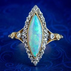 A striking antique opal navette cluster ring from the late 19th Century built around a mesmerising natural opal cabochon in the centre (approx. 2.5ct) that has been marquise-cut to match the gallery.  The opal displays a beautiful medley of colours that fade and intensify with the light and is framed by twinkling rose-cut diamonds around the border, with an additional diamond on each shoulder (approx. 0.28ct total).  Opal is the birthstone of October. Their magic has been revered throughout hist Luxury Victorian Gold Opal Ring, Antique Opal Ring, Floral Engraving, Edwardian Engagement Ring, Antique Jewelry Rings, Estate Rings, Gold Eagle, Diamond Settings, Memento Mori